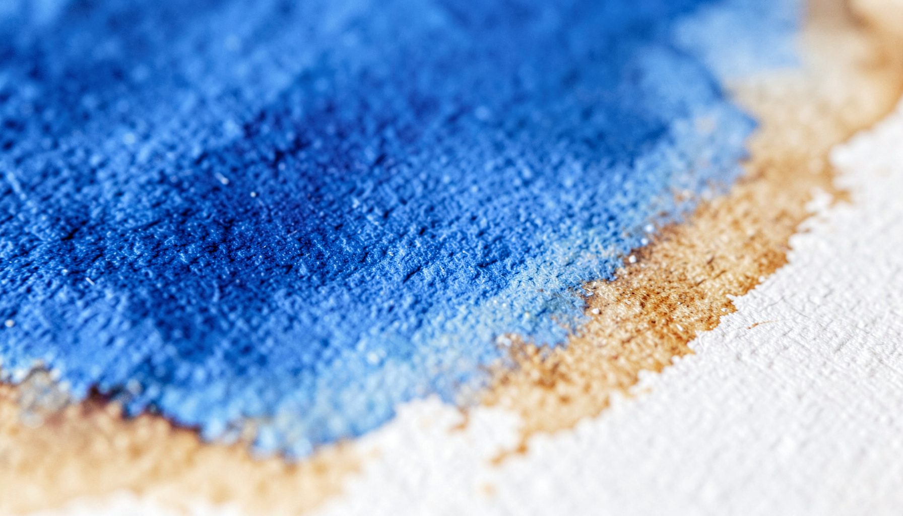 An extreme close-up of textured watercolor paper with soft washes of indigo and burnt sienna bleeding at the edges