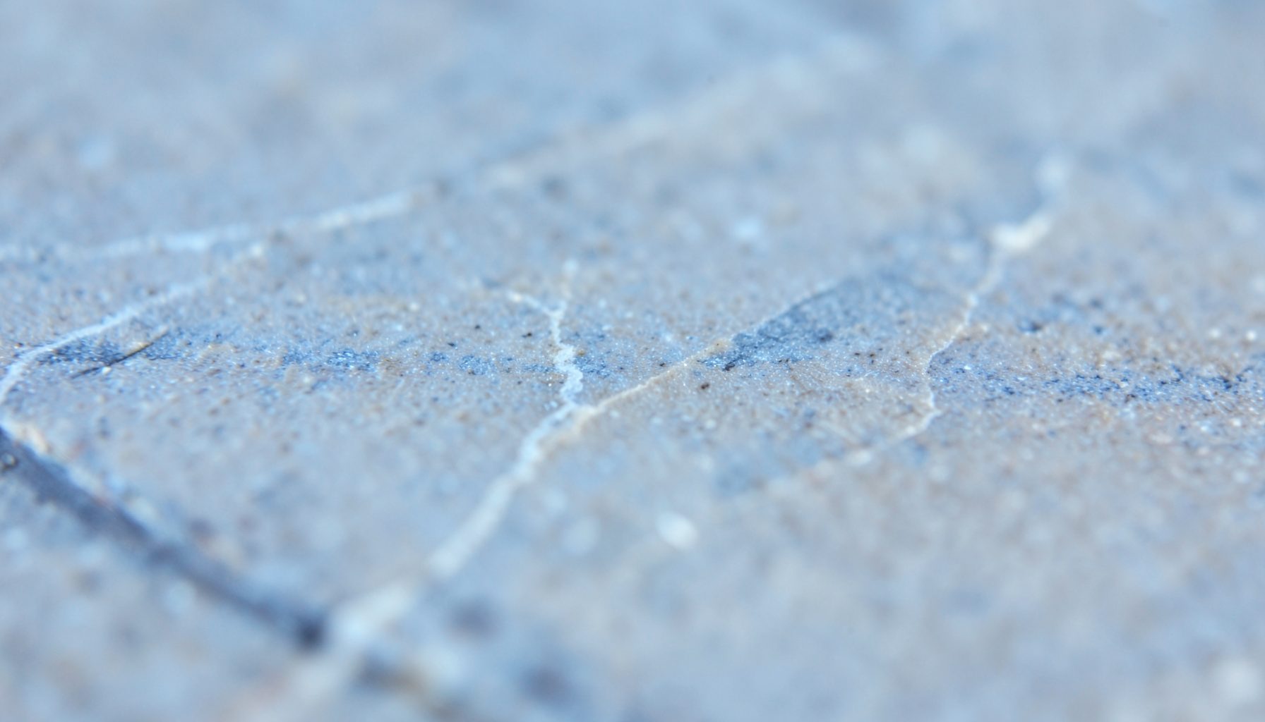 A macro photograph of smooth stone tile, soft dove grey with faint mineral veins in lighter silver tones.
