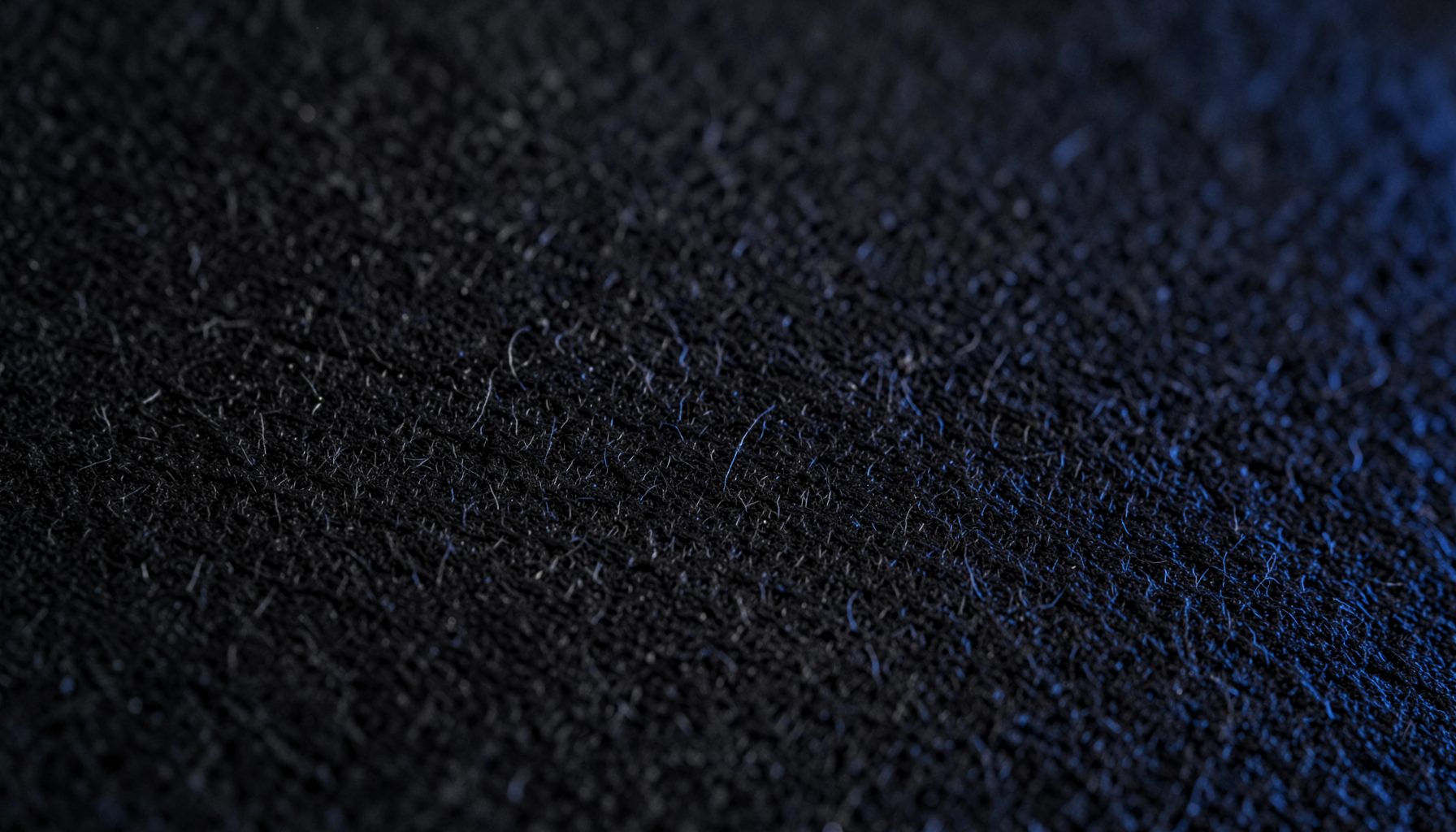 Extreme close-up of matte black paper grain with subtle fibrous texture, deep charcoal tones, and a soft velvety surface catching faint directional light.
