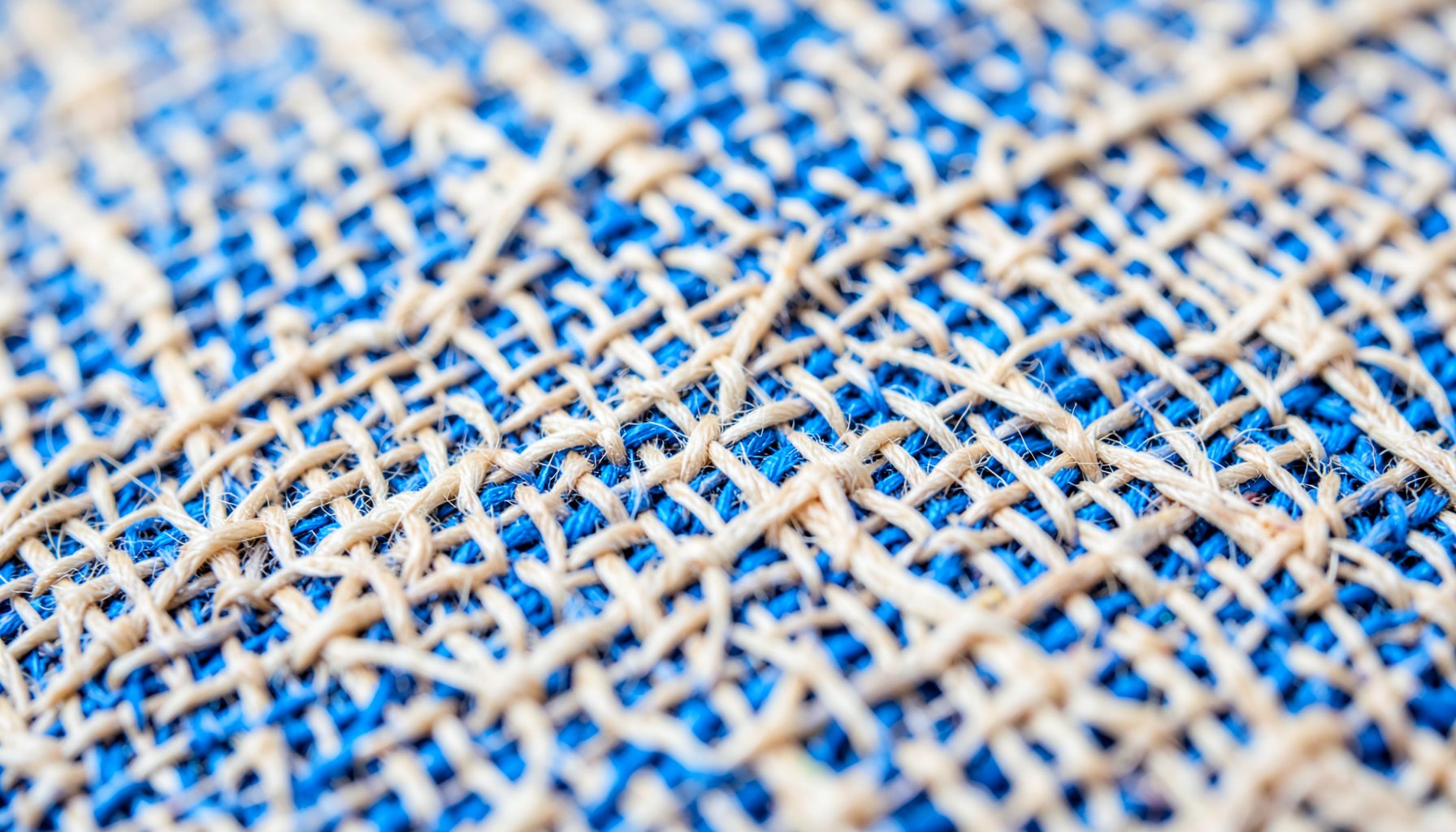 An extreme close-up of woven linen fabric, showing natural beige and cream threads crossing in an organic grid.