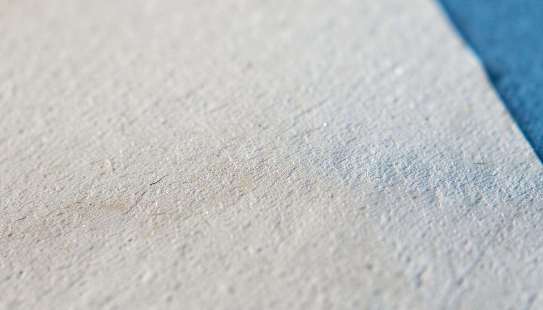 A close-up photograph of textured matte paper with subtle grain, in muted warm greys and off-white tones.