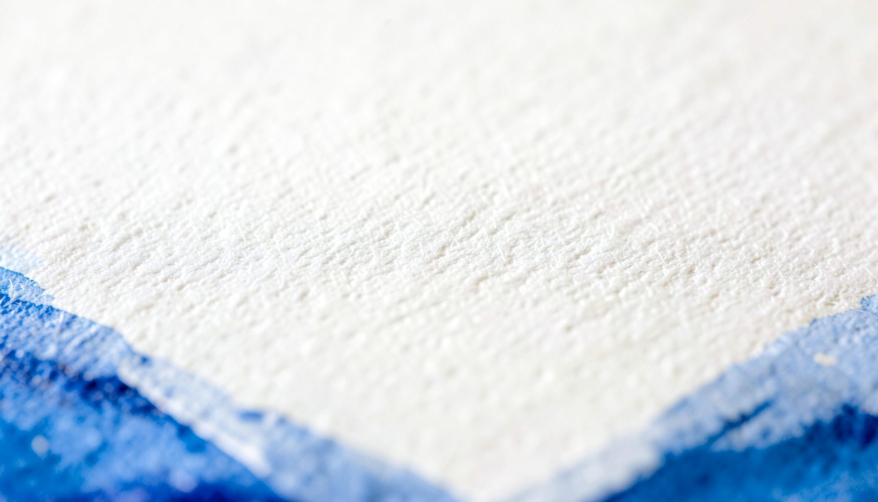 A tight macro shot of heavyweight watercolor paper, creamy white with a soft toothy grain under raking light.