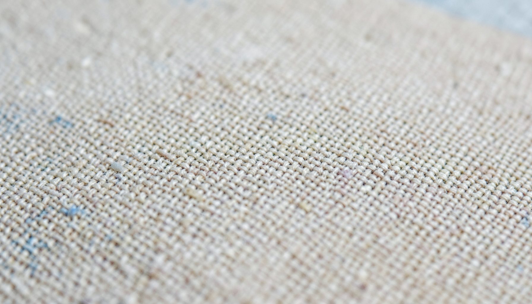 Close-up of coarse canvas texture in muted beige and cream tones with an understated artistic mood