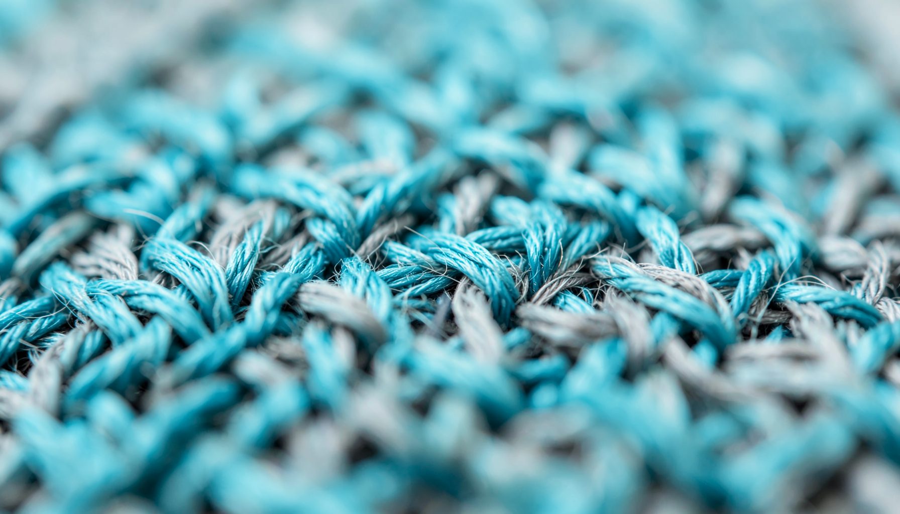 Macro shot of woven textile fibers in soft teal and grey tones with a tactile, refined mood