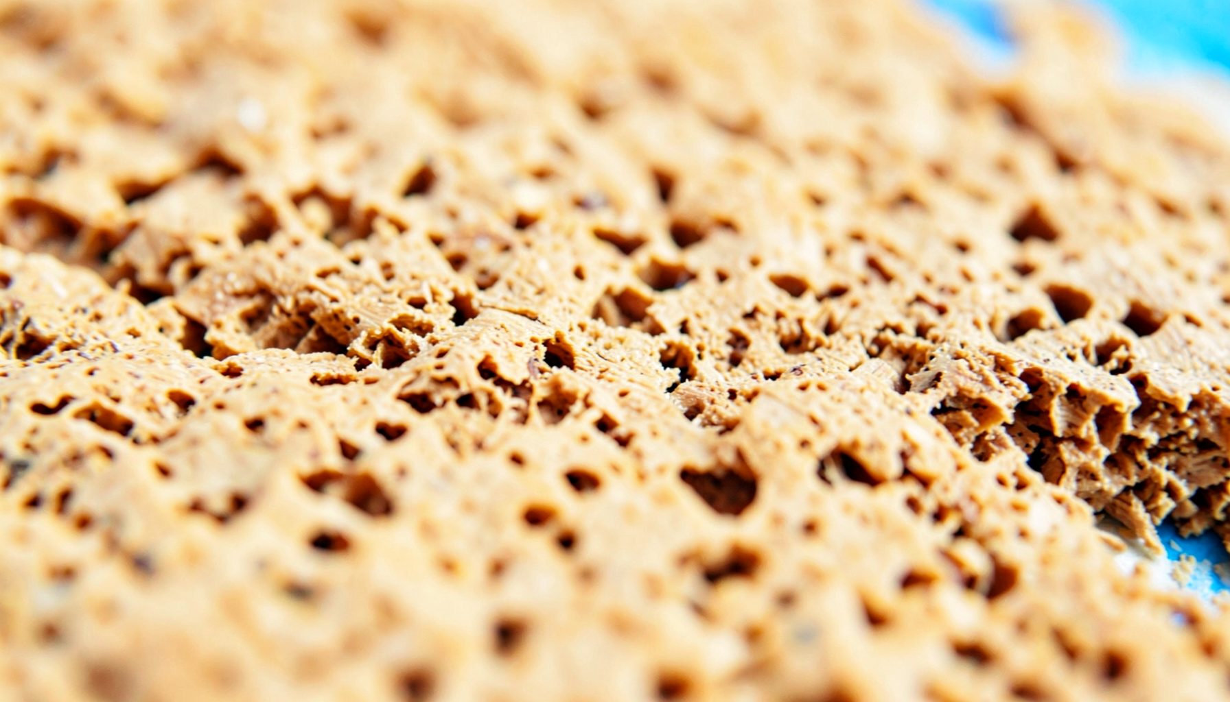 A macro photograph of raw cork surface, warm tan and ochre tones with irregular porous texture.